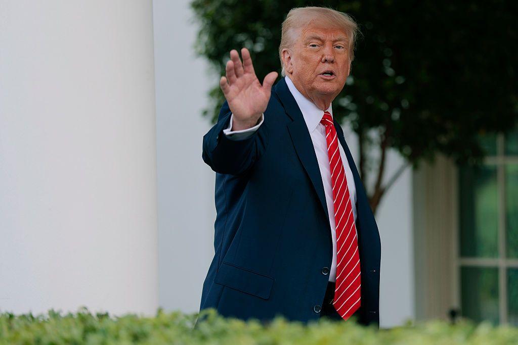 El presidente de Estados Unidos, Donald Trump, saluda desde la Casa Blanca. Viste un traje azul marino y una corbata roja con rayas blancas.