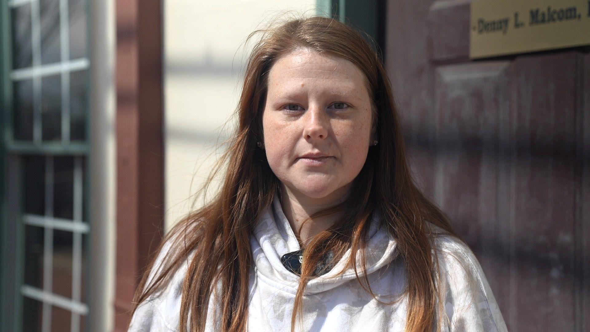 Joy Coker mira directamente a la c&aacute;mara, con una sudadera blanca con capucha y el pelo suelto ondeando al viento.