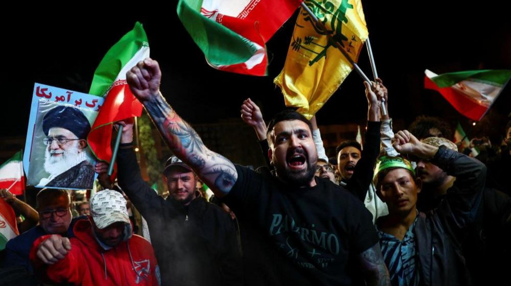 Hombres en Teher&aacute;n con s&iacute;mbolos de la Rep&uacute;blica Isl&aacute;mica levantan los brazos en signo de victoria.