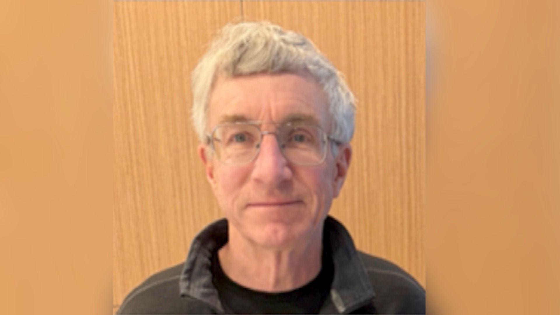 Una foto de William, que tiene el pelo blanco, gafas y una chaqueta con cuello.