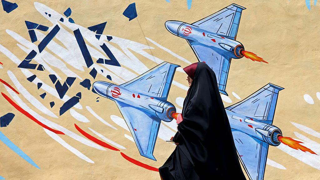 Se puede ver a unos drones destrozando una Estrella de David mientras una mujer vestida de negro pasa junto a un mural antiisrael&iacute; en Teher&aacute;n.