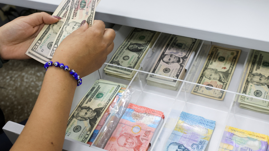 Una mujer con una pulsera azul cuenta d&oacute;lares de un caj&oacute;n abierto.