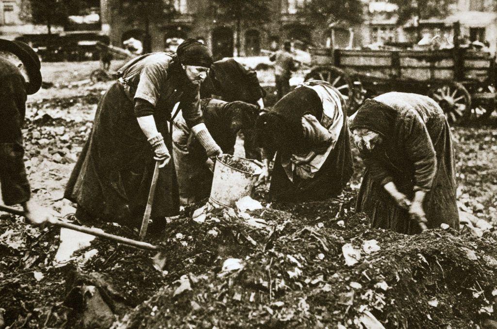 Un grupo de mujeres con cubos y azadas agachadas sobre un mont&oacute;n de basura en una foto de &eacute;poca. 