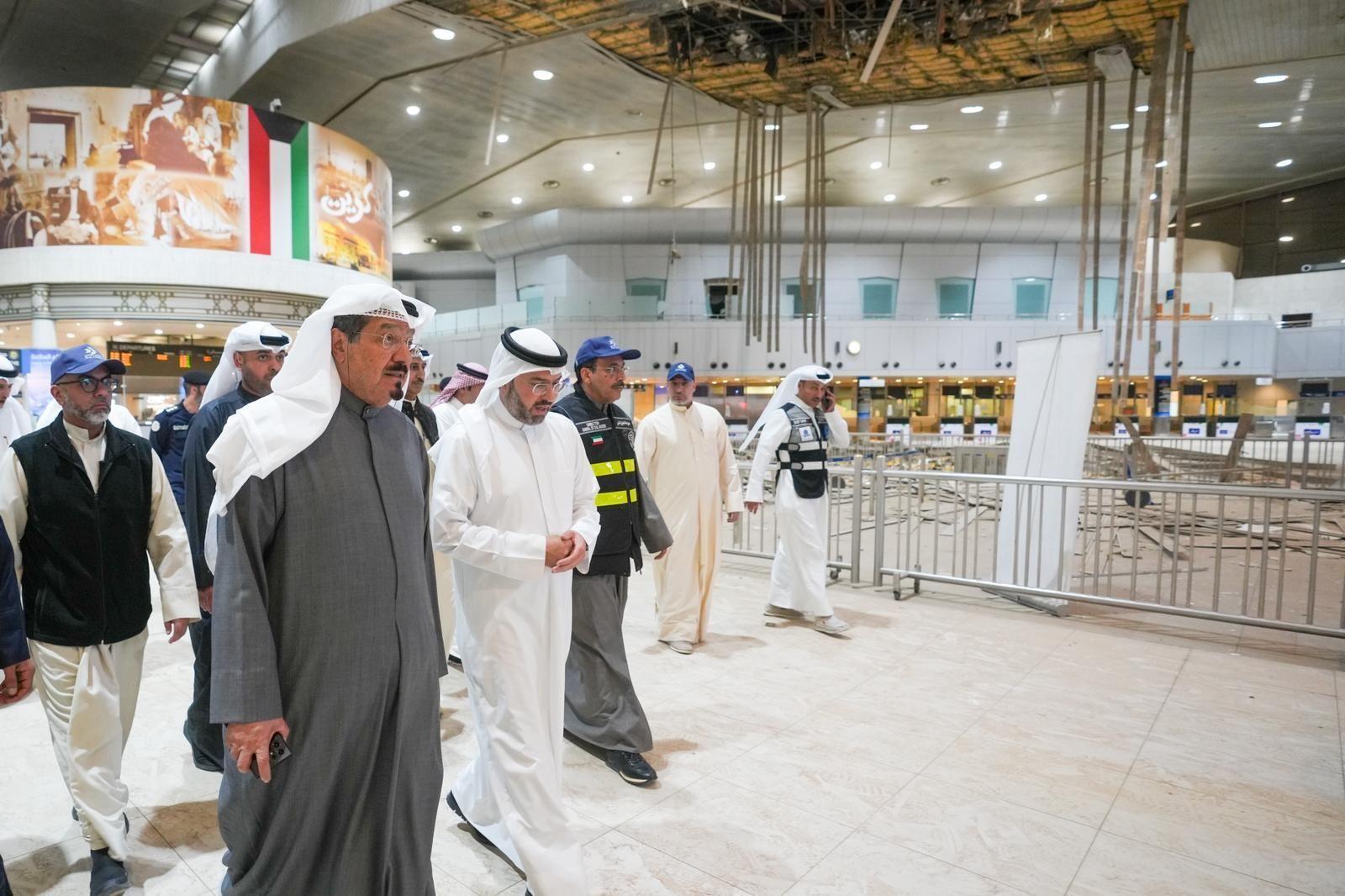 Ahmad al Abdullah al Sabah camina con otros dignatarios por el edificio terminal del aeropuerto, junto a una zona acordonada donde se observan da&ntilde;os. El techo presenta deterioros, con baldosas retiradas y estructuras colapsadas.