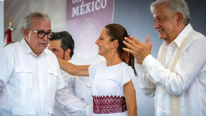 La presidenta de M&eacute;xico coloca su brazo sobre el gobernador Rocha Moya, mientras que AMLO aplaude.