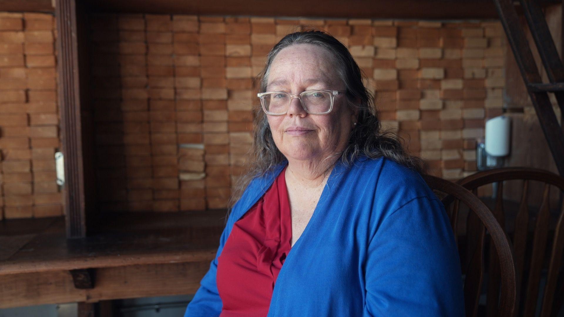 Gareth Fenley est&aacute; sentada en un caf&eacute; con un c&aacute;rdigan azul sobre una camisa roja.
