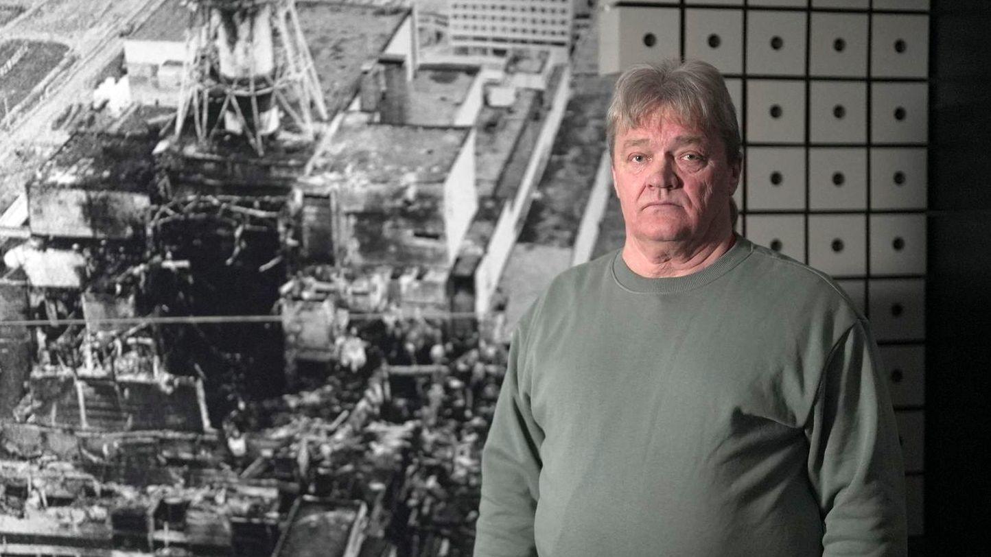 Nikolai Solovyov, ingeniero jefe de la sala de turbinas en el momento del accidente, fotografiado frente a una imagen del reactor destruido, en el museo de Slavutych. Tiene el pelo canoso, lleva una sudadera de color gris verdoso y mira a la c&aacute;mara con expresi&oacute;n seria.