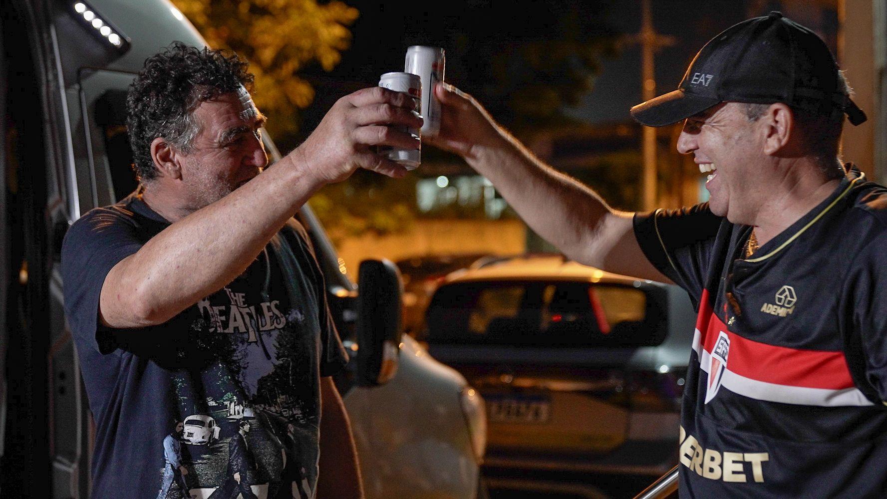 Dos hombres brindan con latas de cerveza.