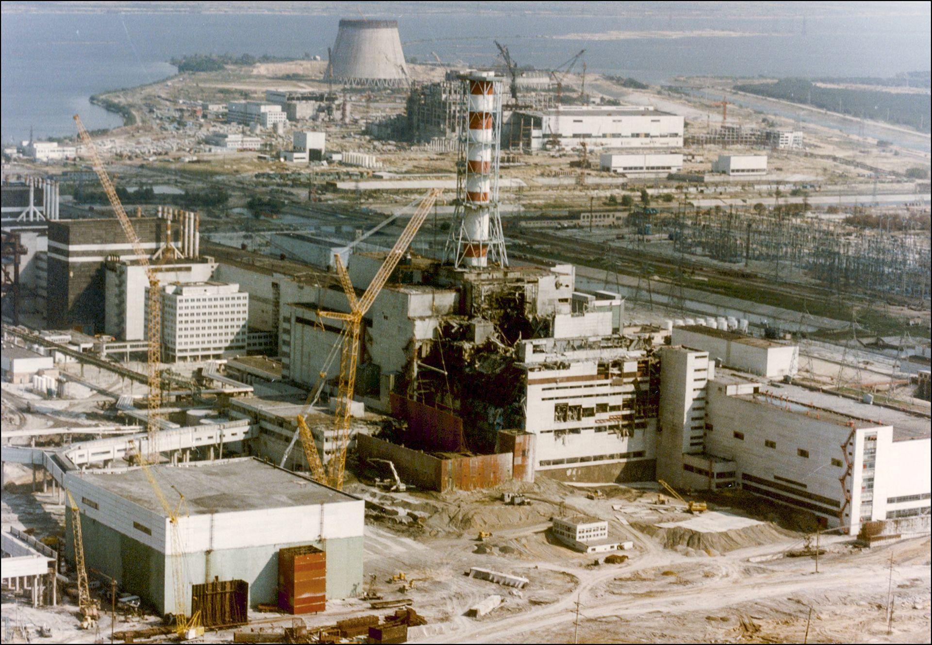 Vista de la central nuclear de Chern&oacute;bil el 29 de abril de 1986, tres d&iacute;as despu&eacute;s de la explosi&oacute;n. El edificio que alberga el reactor n&uacute;mero 4 presenta graves da&ntilde;os, con escombros ennegrecidos bajo una chimenea roja y blanca.