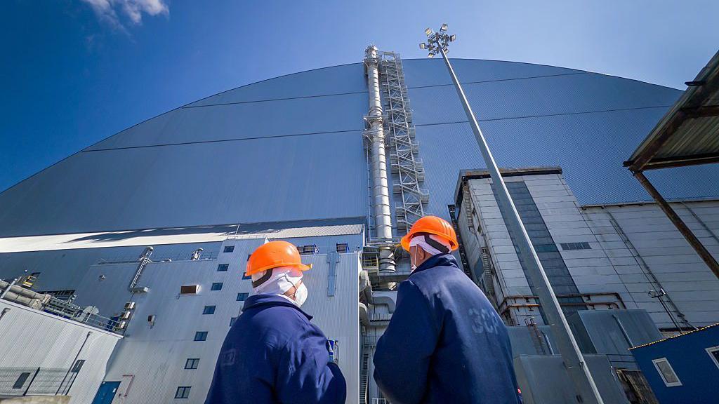 El arca de protecci&oacute;n frente al cual se encuentran dos trabajadores con cascos naranjas.