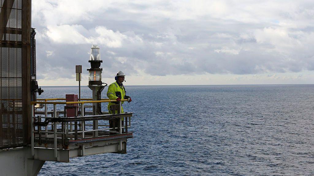 Un hombre observa la lejan&iacute;a en un saliente de una plataforma en el mar. 
