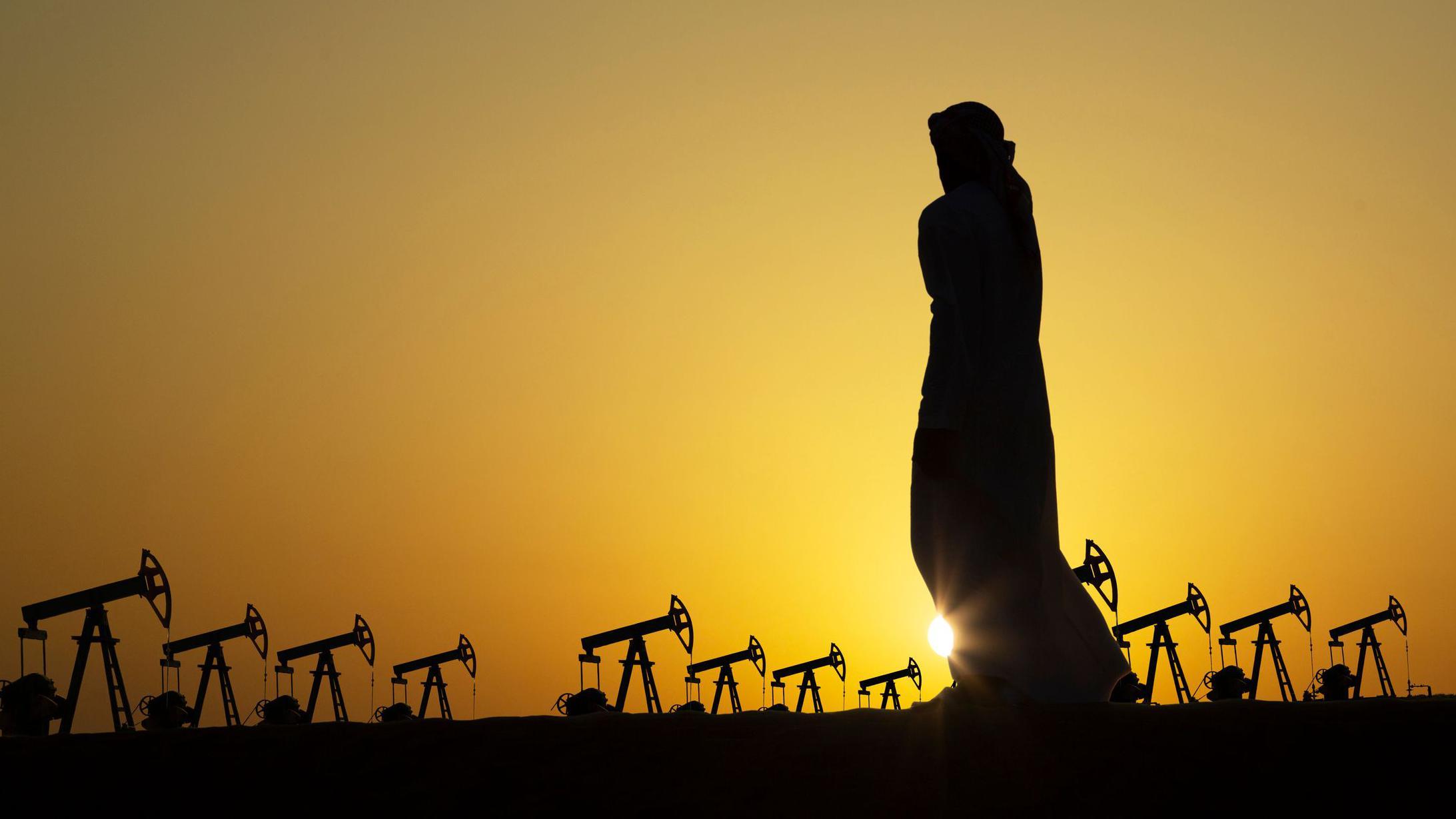 La silueta de un hombre &aacute;rabe observa decenas de unidades de bombeo de petr&oacute;leo contra la puesta del Sol