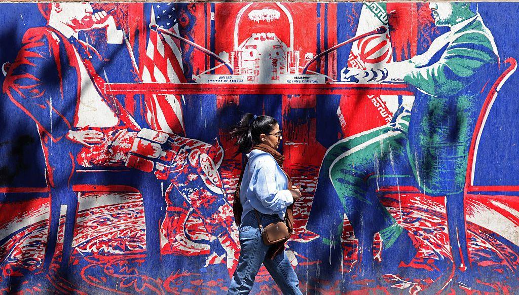 Una mujer pasa frente a un mural antinorteamericano de colores vivos que representa las conversaciones entre Ir&aacute;n y Estados Unidos. 