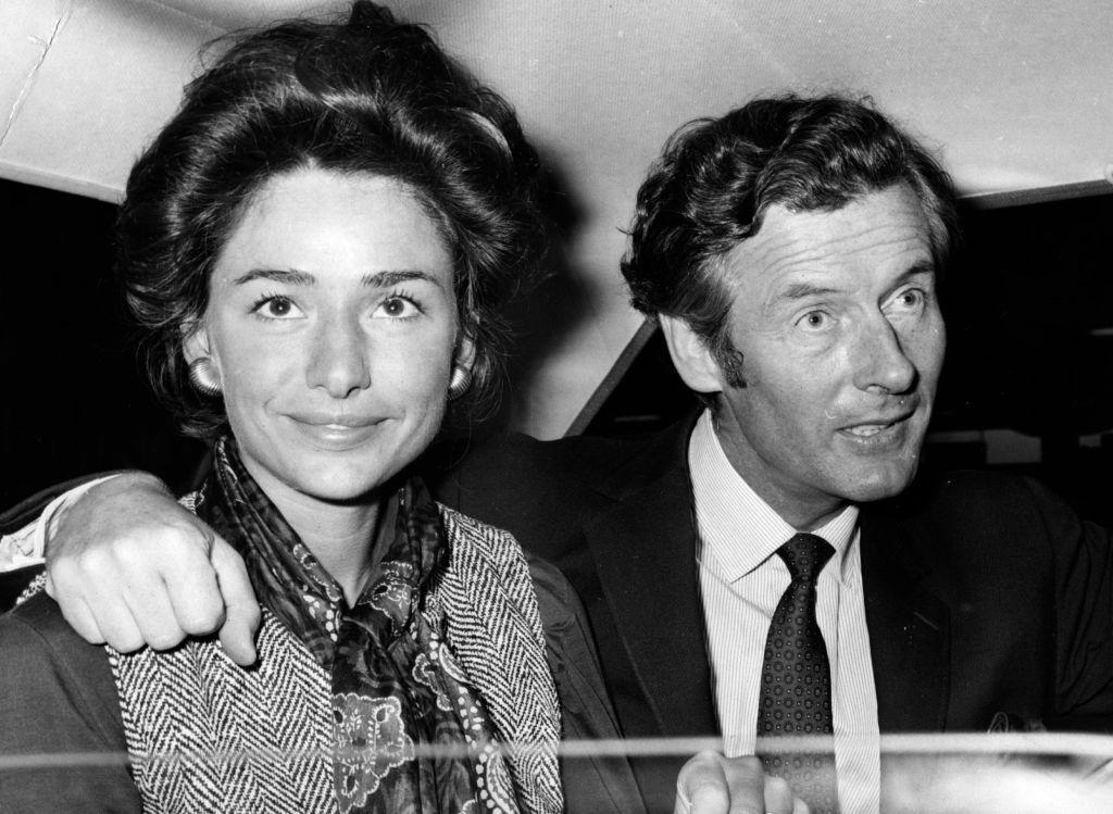 Una pareja dentro de un autom&oacute;vil. El hombre tiene el brazo sobre el hombro de la mujer, que est&aacute; mirando directamente a c&aacute;mara.