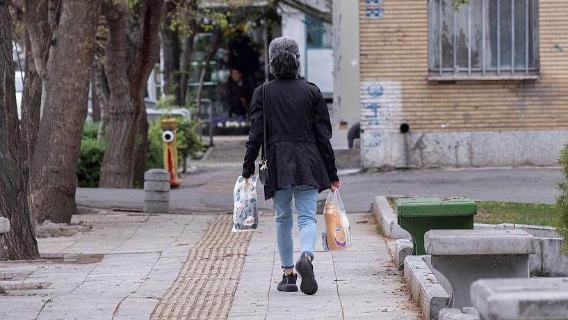 Una mujer camina por la acera llevando bolsas de la compra.