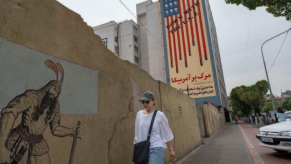 Una joven iran&iacute; camina por una acera bajo un mural antiestadounidense en el centro de Teher&aacute;n, Ir&aacute;n.

