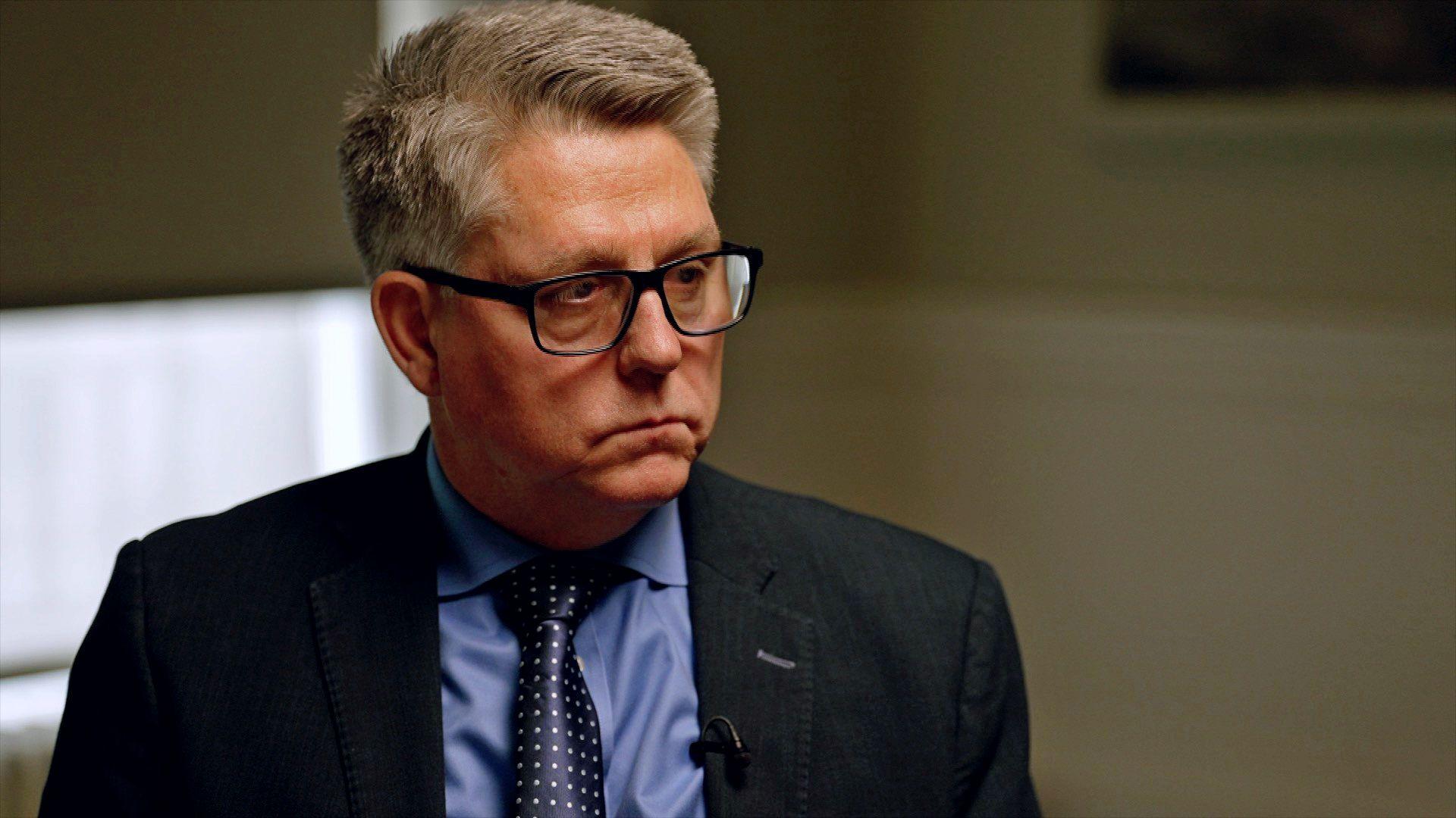 Kevin Hyland sentado, vestido de traje oscuro y con lentes, durante la entrevista con la BBC.