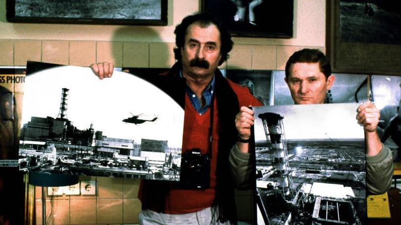 Dos hombres sostienen dos im&aacute;genes de la planta de Chern&oacute;bil tomadas desde un helic&oacute;ptero. 