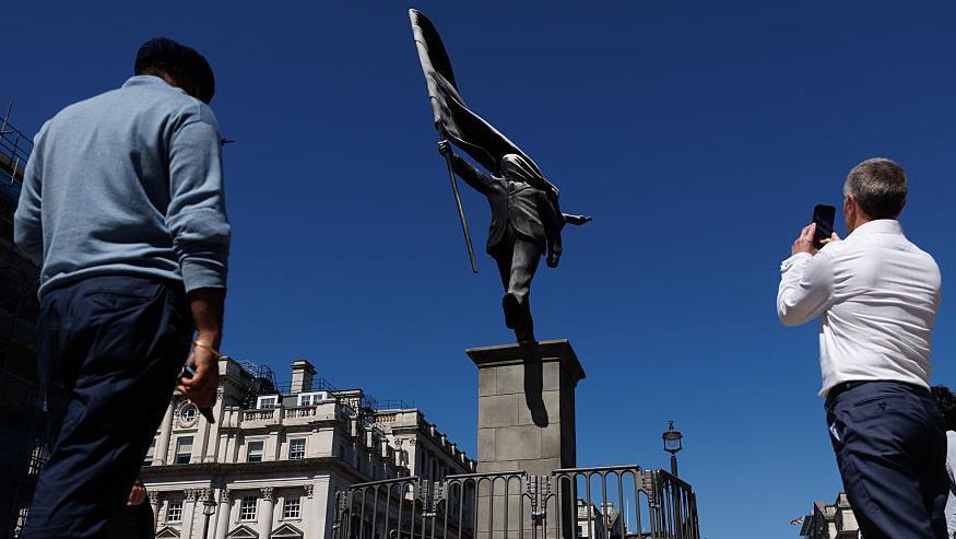 Personas tomando im&aacute;genes de la estatua con sus tel&eacute;fonos celulares. 