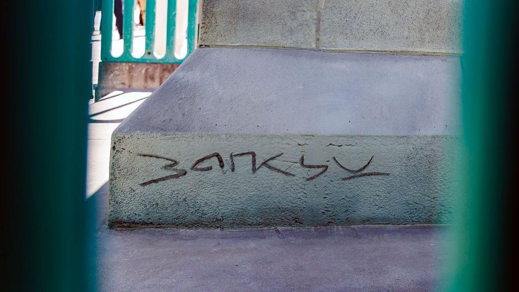 La firma de Banksy grabada en el z&oacute;calo de la estatua. 