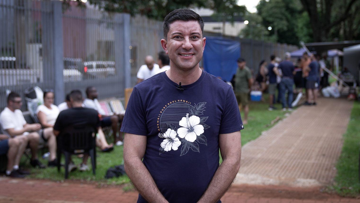 Cornelio Melgarejo, un hombre joven, con una playera azul estampada con flores blancas, est&aacute; parado frente a una fila de brasile&ntilde;os que buscan solicitar residencia en Paraguay.