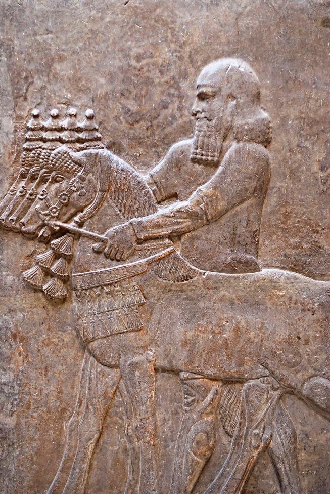 La figura de un hombre esculpida en piedra. De cuerpo entero, se encuentra de perfil con un caballo. A lo largo se ven m&aacute;s caballos.