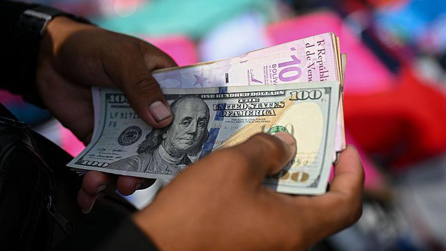 Un hombre sujeta unos billetes de d&oacute;lares y bol&iacute;vares.