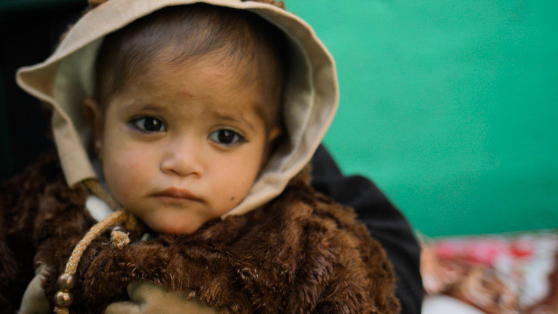 Una ni&ntilde;a peque&ntilde;a, vestida con un jersey marr&oacute;n grueso y con una capucha beige en la cabeza, mira a la c&aacute;mara