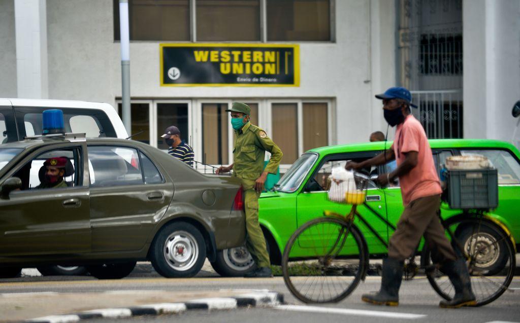 Autos y personas parados en una calle donde se ve una sucursal de Western Union en La Habana. 