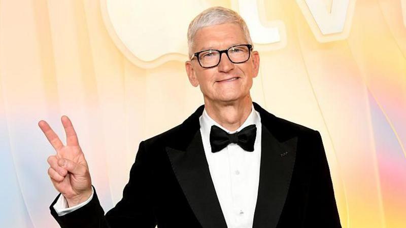 Tim Cook, con corbat&iacute;n y traje negro, hace la se&ntilde;al de paz con sus dedos.