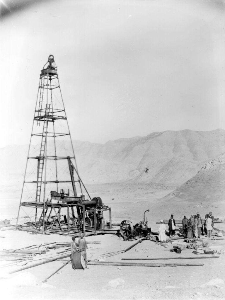Una foto en blanco y negro muestra la construcci&oacute;n de una primitiva torre de extracci&oacute;n de petr&oacute;leo en una regi&oacute;n des&eacute;rtica con unas diez personas alrededor