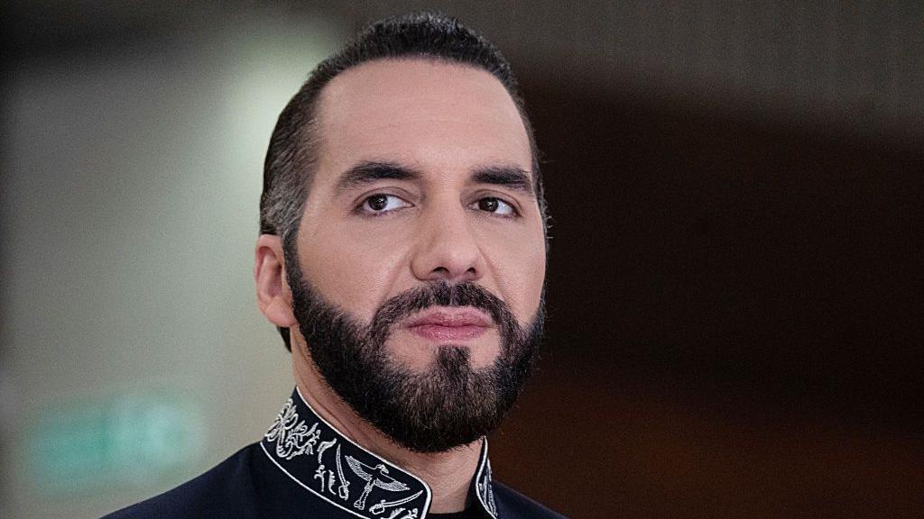 imagen de nayib bukele, presidente de El Salvador. Mira a la c&aacute;mara con rostro serio. Tiene barba y lleva el cabello hacia atr&aacute;s. Tiene una camisa negra. 