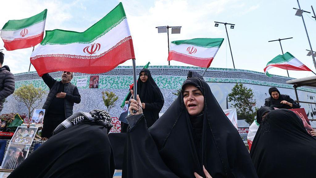 Mujeres iran&iacute;es ondean banderas nacionales mientras la gente se re&uacute;ne en la Plaza de la Revoluci&oacute;n de Teher&aacute;n despu&eacute;s de que Estados Unidos e Ir&aacute;n acordaran un alto el fuego de dos semanas.