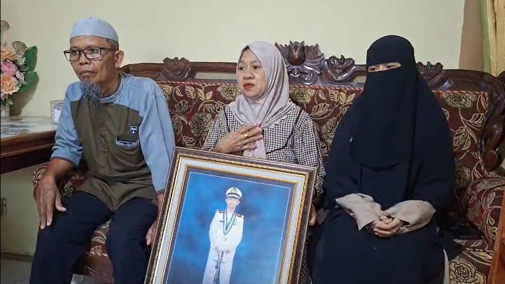 La familia del capit&aacute;n Ashari Samadikun en Indonesia sentada en un sof&aacute; durante una entrevista. La mujer en el centro sostiene un retrato grande de &eacute;l enmarcado.