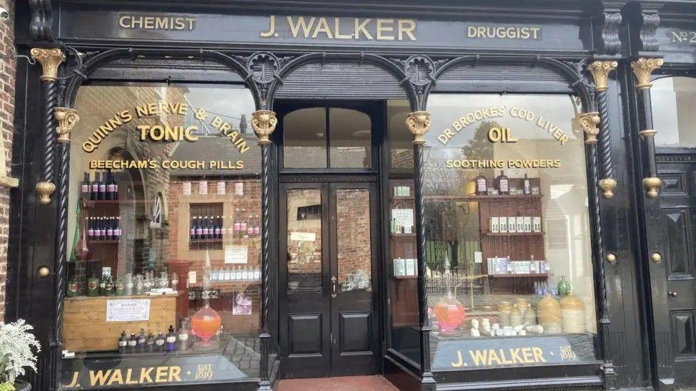 Un escaparate verde y dorado con las palabras "J Walker", "qu&iacute;mico" y "farmac&eacute;utico"