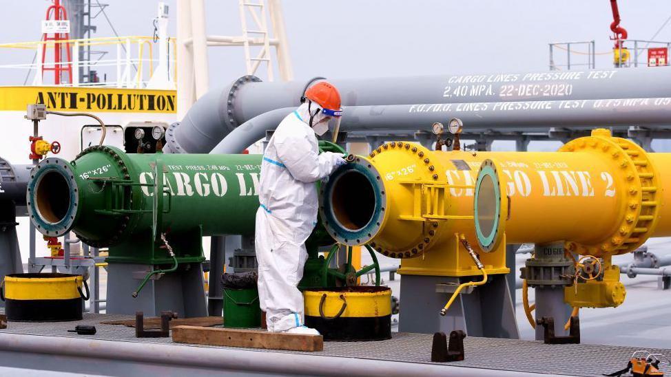 Un hombre revisa dos tubos, uno amarillo y otro verde, en una refiner&iacute;a china. 