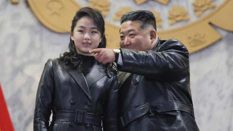 Con su larga melena recogida, Kim Ju Ae permanece de pie junto a Kim Jong Un, quien se&ntilde;ala con el dedo, ambos vestidos con chaquetas negras de cuero con cintur&oacute;n a juego.