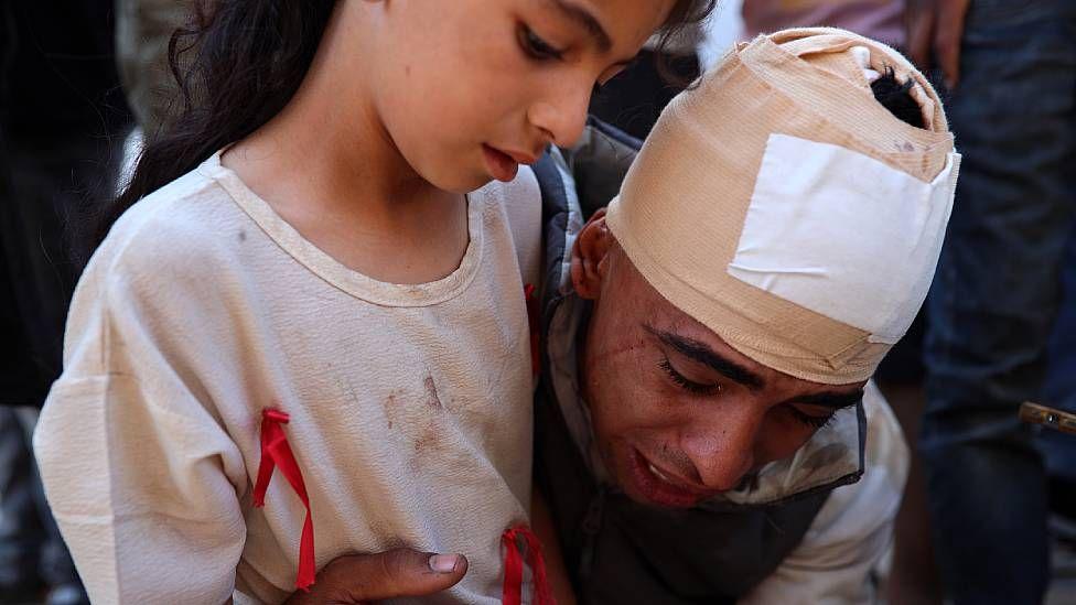 El esposo de Shaima Al-Shawish, con la cabeza vendada, llora abrazando a su hija de unos 10 a&ntilde;os mientras observa los restos de su mujer. 
