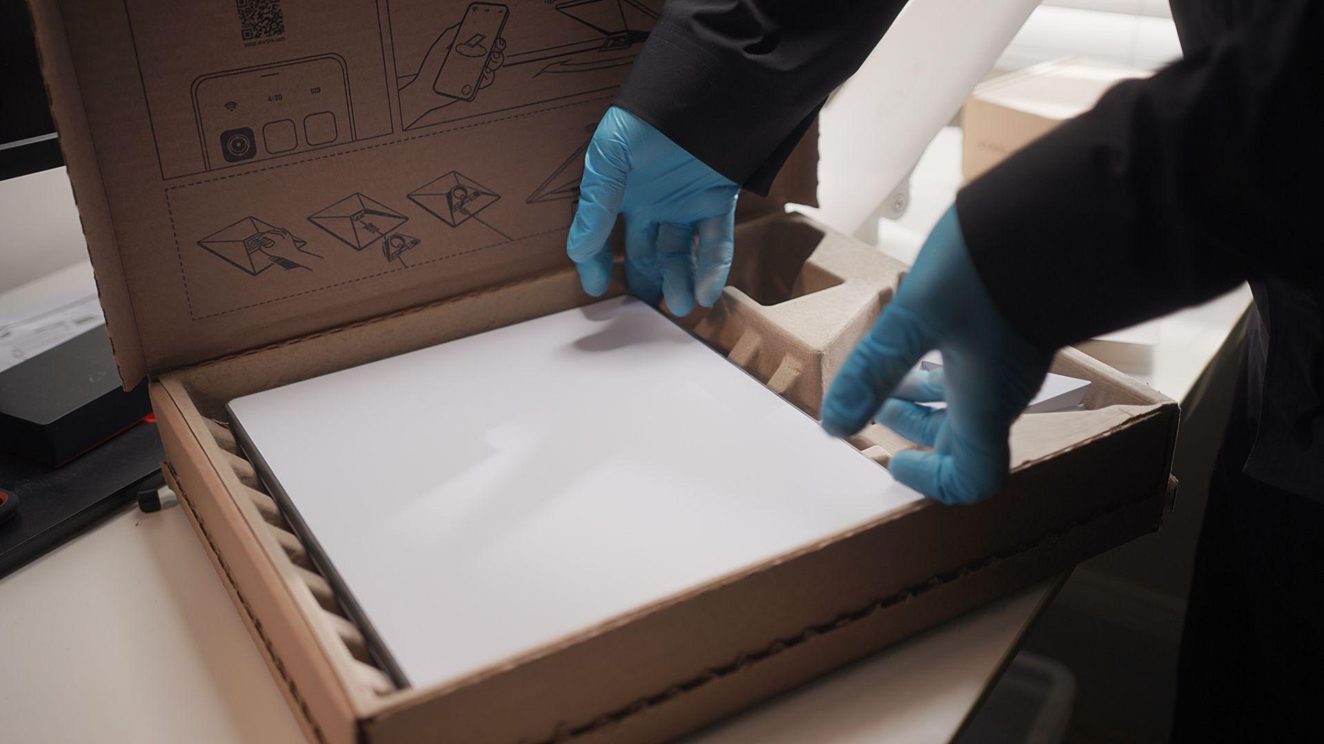 Un dispositivo de Starlink, de color blanco y forma rectangular que est&aacute; siendo preparado por una persona, de la que solo se ve sus manos con guantes de goma azules.