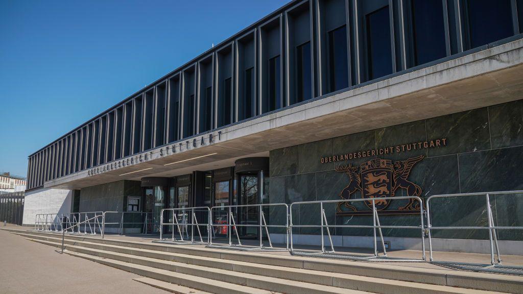 Un edificio con muros de piedra verde y gris, con un emblema dorado en el lateral que reza &laquo;Oberlandesgericht Stuttgart&raquo;.