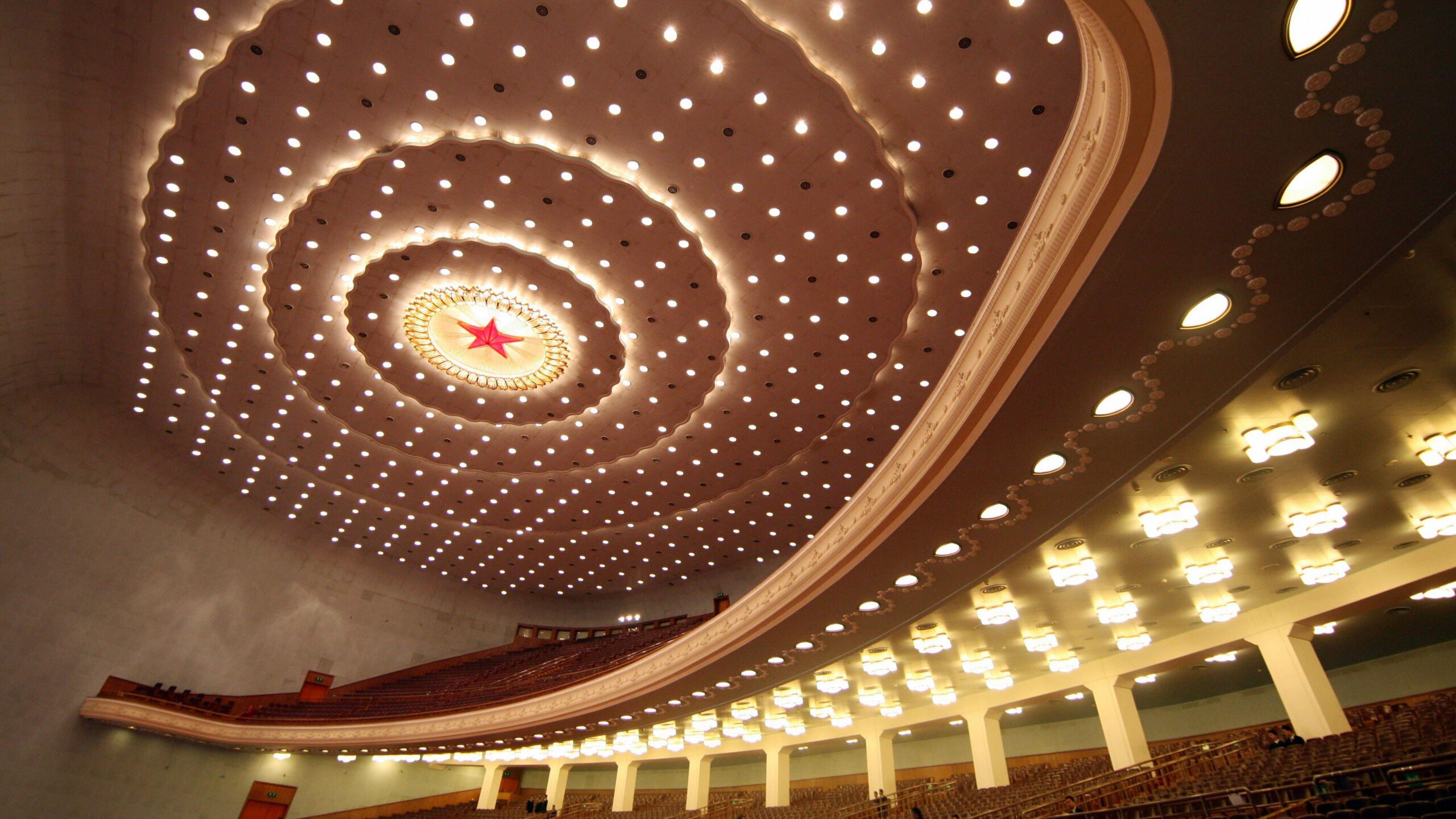 Una fotograf&iacute;a tomada al interior de un auditorio, mirando hacia un techo repleto de luces circulares blancas y una estrella roja con un c&iacute;rculo iluminado en el centro; se aprecian filas de asientos dispuestas en varios niveles.