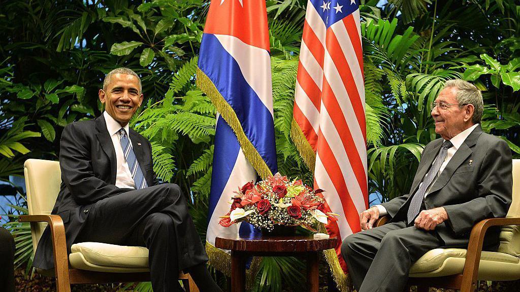 Los presidentes Barack Obama y Ra&uacute;l Castro sonr&iacute;en sentados en La Habana junto a las banderas de EE.UU. y Cuba, durante el proceso de normalizaci&oacute;n de relaciones bilaterales en 2016. 
