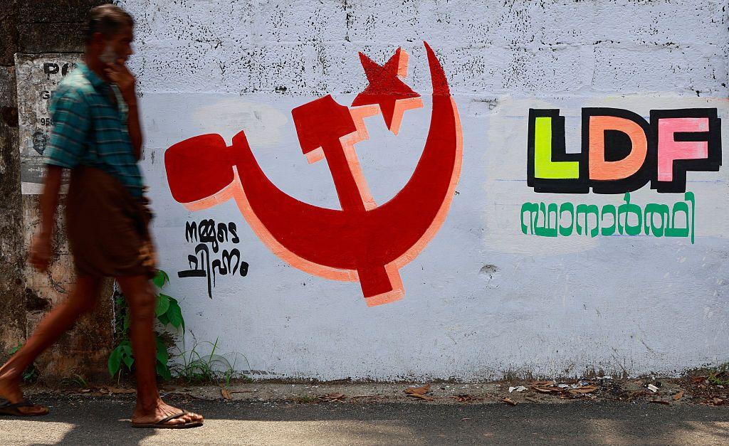 Un hombre pasa junto a un muro al borde de la carretera con grafitis electorales del Partido Comunista de India (Marxista) 