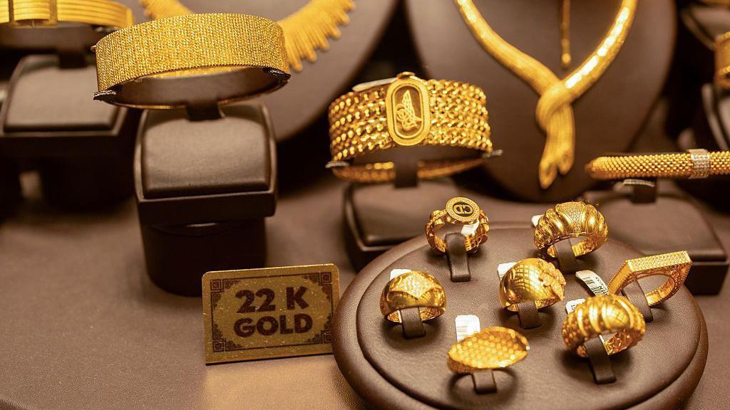 Se exhiben dos brazaletes de oro (izquierda) y siete anillos de oro. Entre ellos hay un letrero que dice "Oro de 22 quilates".