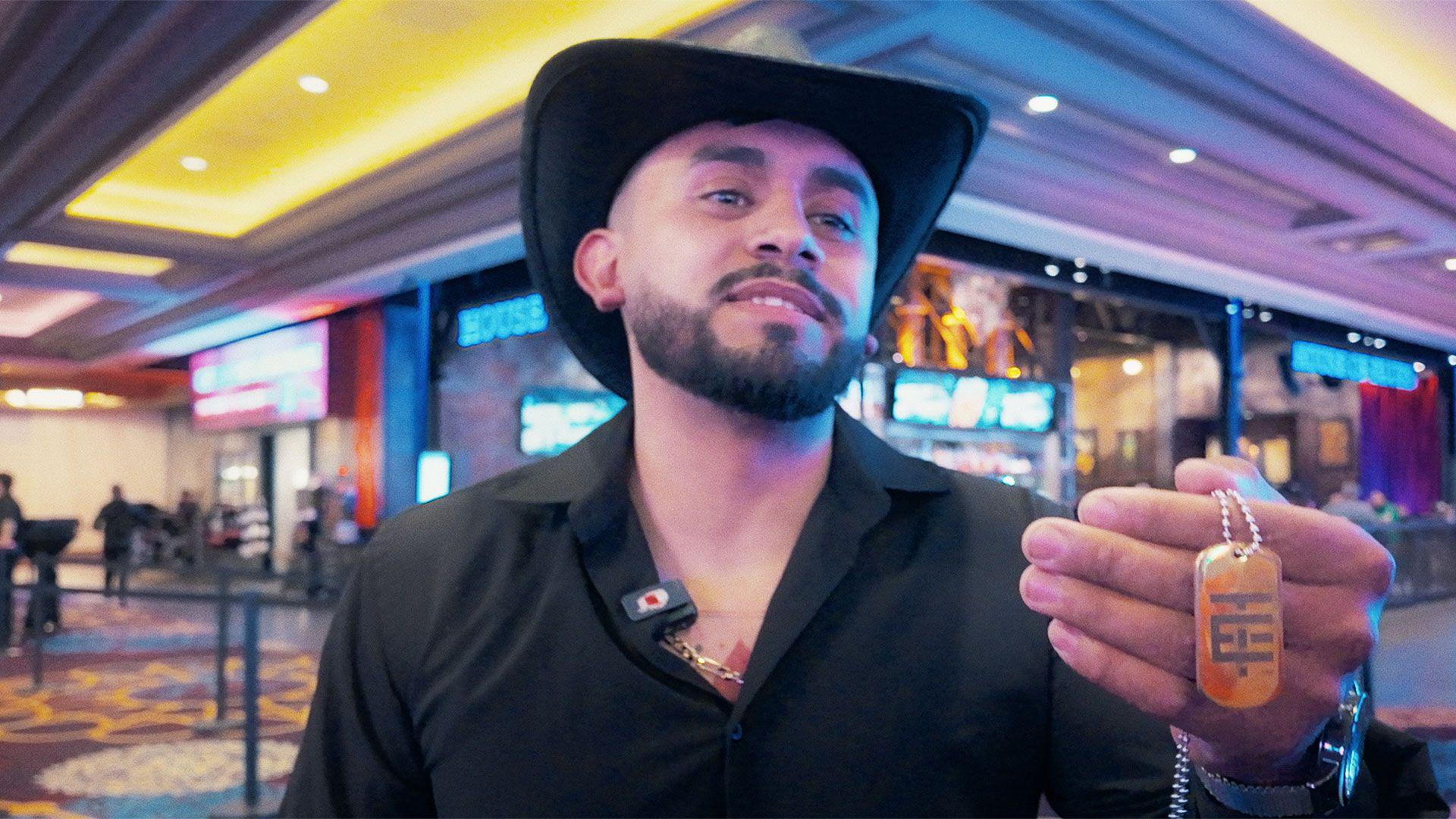 Un fan de El Temach lleva una camisa negra de cuello abierto y un sombrero Stetson negro, y sostiene una cadena especial que le compr&oacute; al influencer como mercanc&iacute;a; es de color naranja con un patr&oacute;n geom&eacute;trico gris.