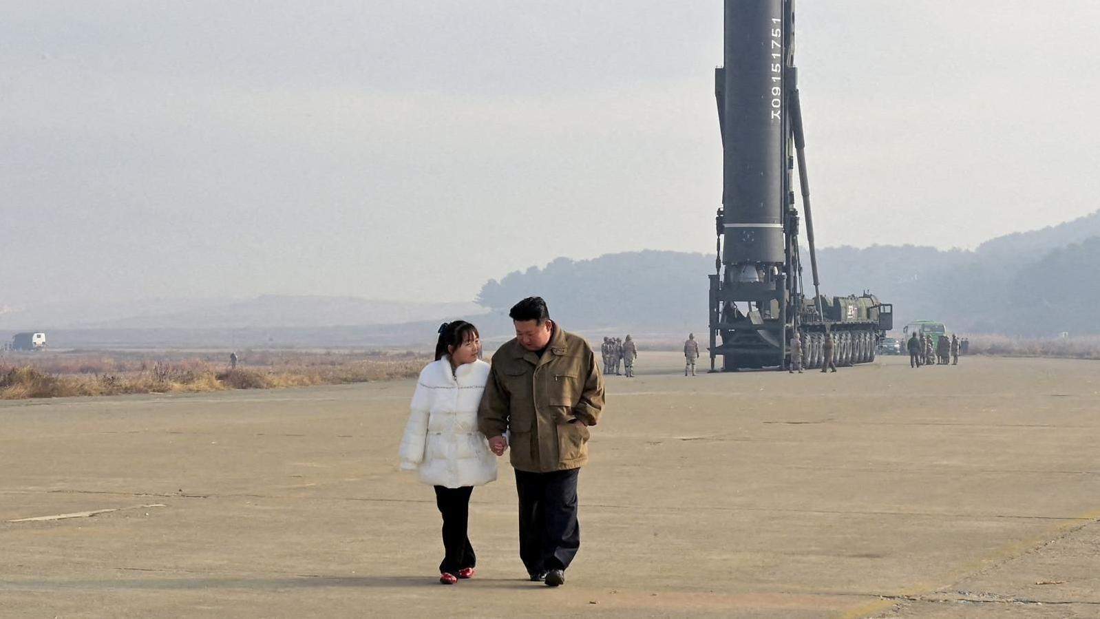 Kim Ju Ae con cabello largo y una chaqueta blanca camina tomada de la mano junto a su padre: Kim Jong Un. Detr&aacute;s se ve una plataforma para lanzar un misil bal&iacute;stico. 