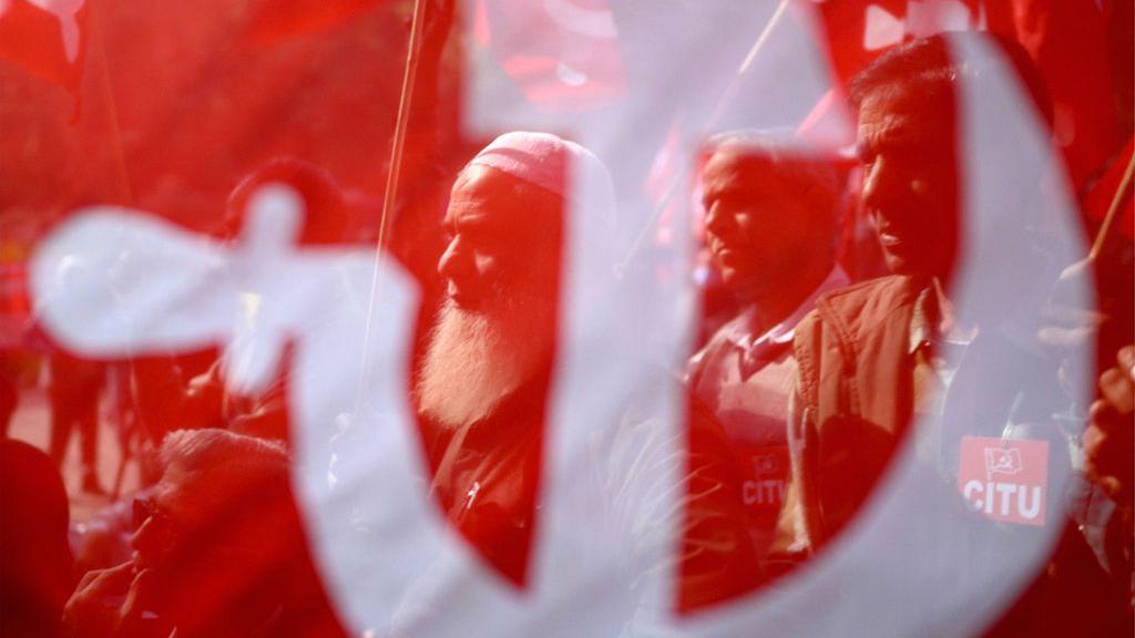 Miembros del sindicato indio vistos a trav&eacute;s de una bandera comunista durante una protesta en Nueva Delhi.