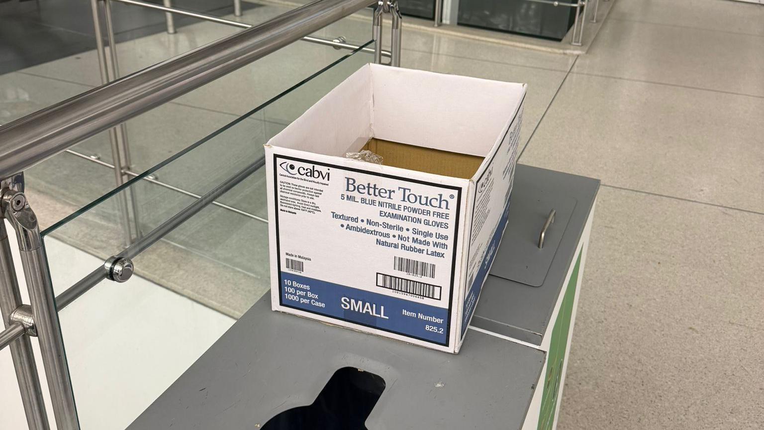 Una caja de cart&oacute;n blanca con texto azul yace sobre una mesa en un aeropuerto. 