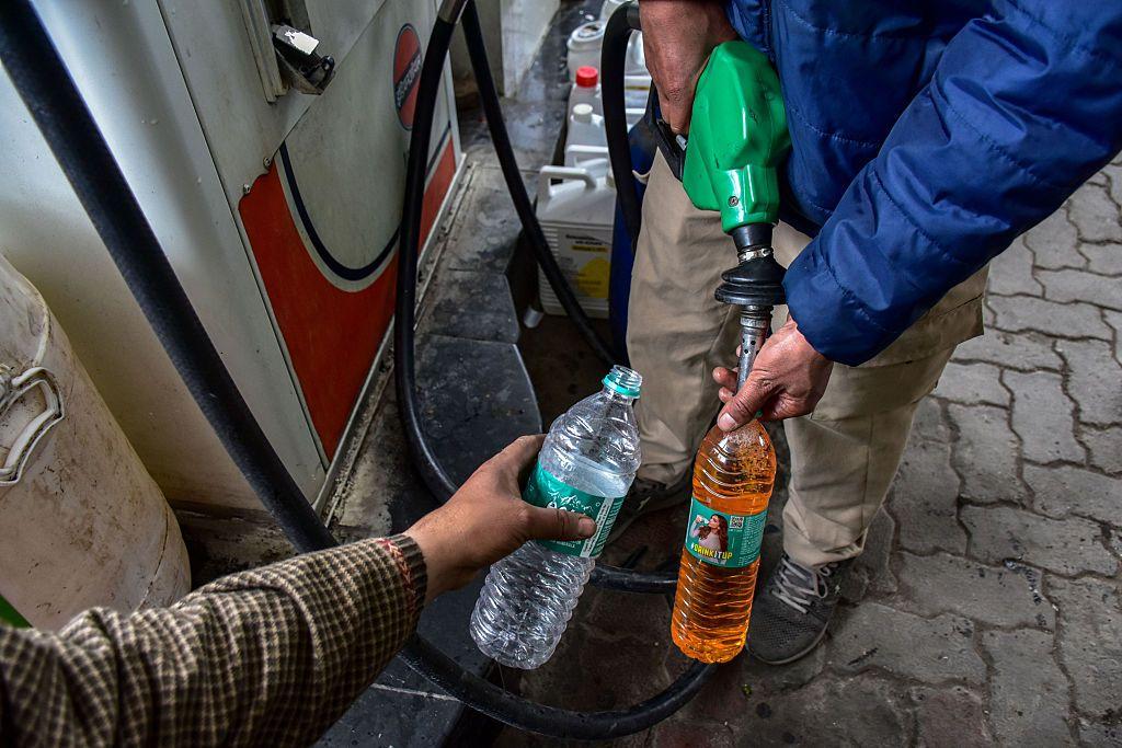 Unos hombres llenan unas botellas con gasolina en una estaci&oacute;n de servicio.