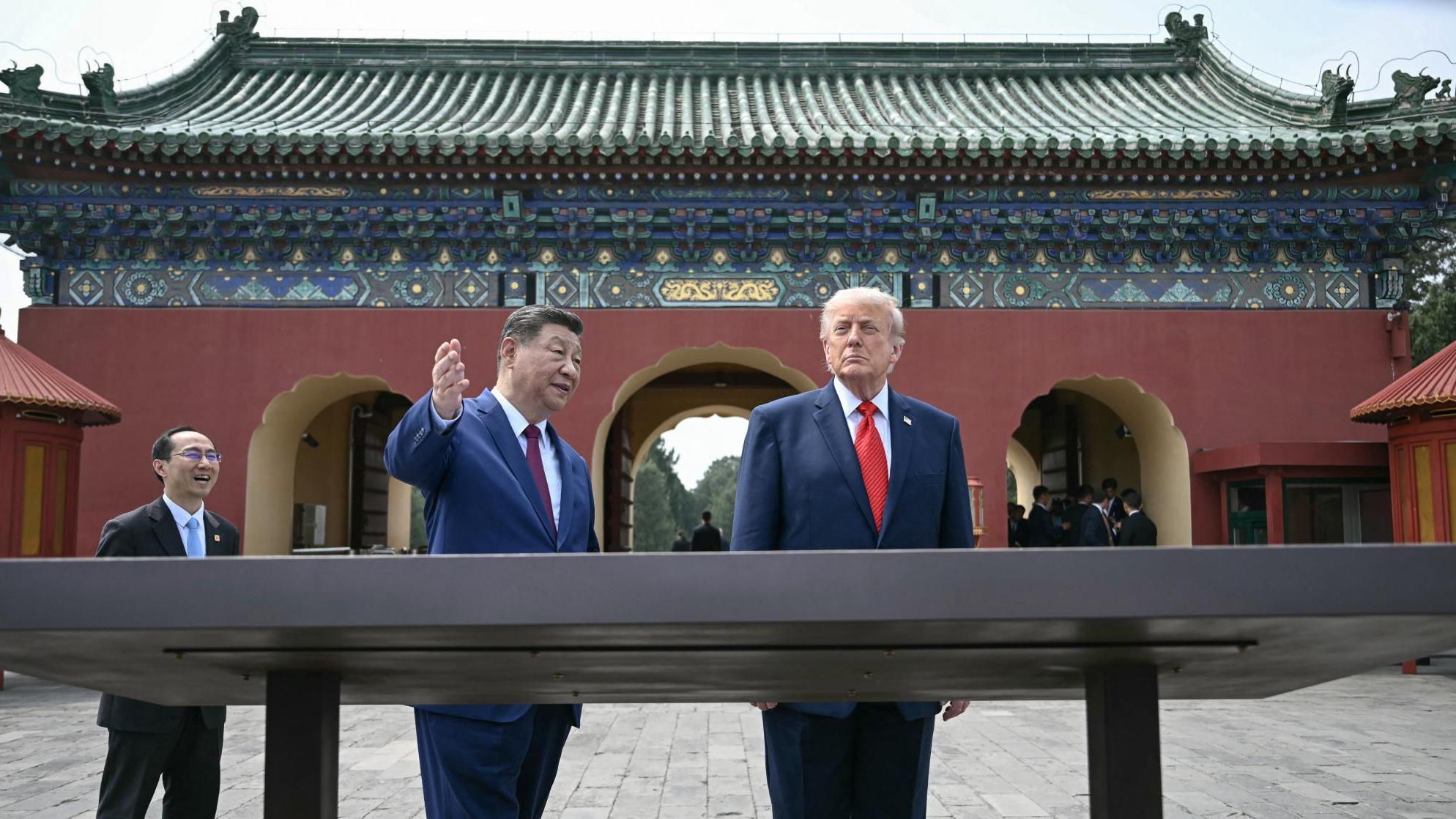 Los presidentes Xi y Trump se encuentran en el patio de un complejo templario, detr&aacute;s de una gran exhibici&oacute;n, con Xi levantando la mano para mostrarle algo a Trump.